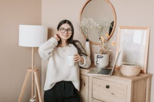 woman with laptop standing at dresser with coffee cup